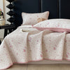 A pink floral quilted bedspread with white piping and a matching pillow is displayed on a dark headboard.