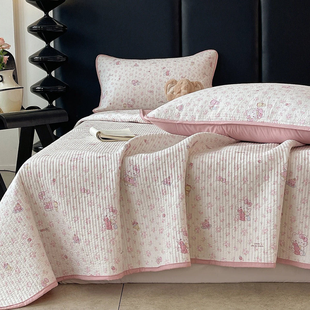 A pink floral quilted bedspread with white piping and a matching pillow is displayed on a dark headboard.