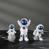 Three handcrafted astronaut figurines in white and blue resin standing on a black marble surface.