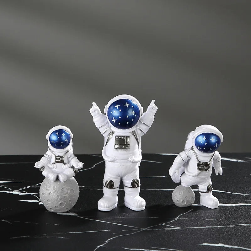 Three handcrafted astronaut figurines in white and blue resin standing on a black marble surface.
