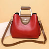 A reddish-brown leather crossbody tote bag with a silver handle and brown strap resting on a light background.