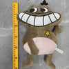 A brown plush toy of an Opila Bird with a wide smile and a yellow star detail, measured against a ruler.