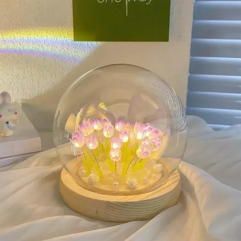 A handcrafted tulip LED night light with pink flowers glows inside a clear glass dome on a wooden base.