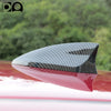 A black shark fin car antenna painted in piano paint, shown in profile against a blurred green background.