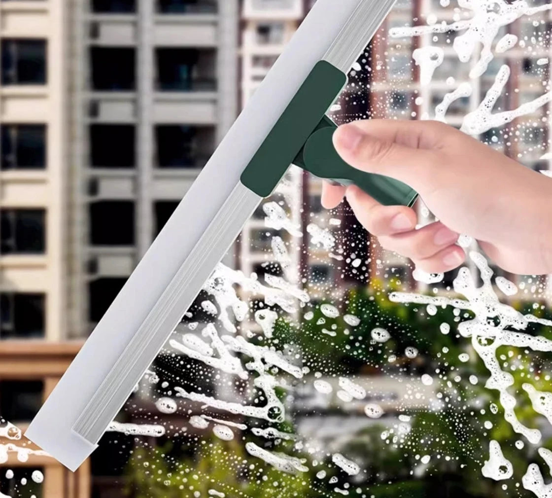 A hand is using a silicone scraper broom and squeegee to clean glass, creating water droplets.