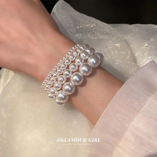 Nahaufnahme einer Hand mit einem eleganten Perlenarmband, vor einem durchsichtigen weißen Hintergrund.