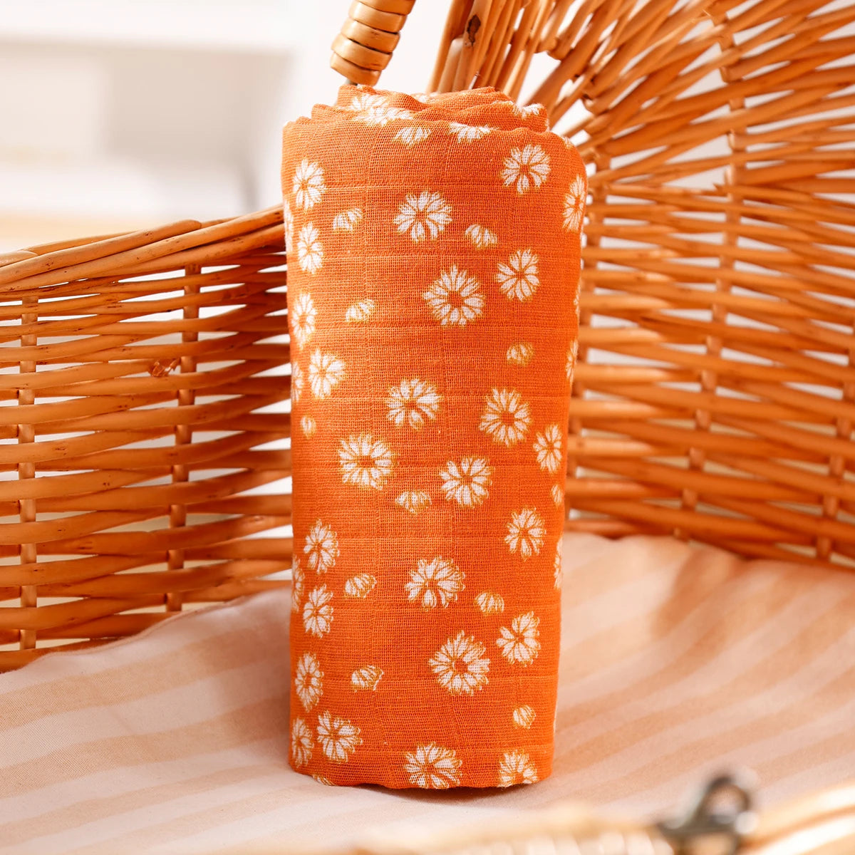 Orange muslin baby swaddle blanket rolled up, resting on a woven basket.