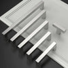 Ein Set moderner Edelstahl-Schubladengriffe diagonal auf einer grauen Oberfläche angeordnet.