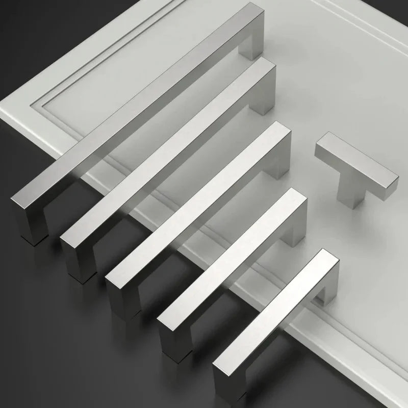 Ein Set moderner Edelstahl-Schubladengriffe diagonal auf einer grauen Oberfläche angeordnet.