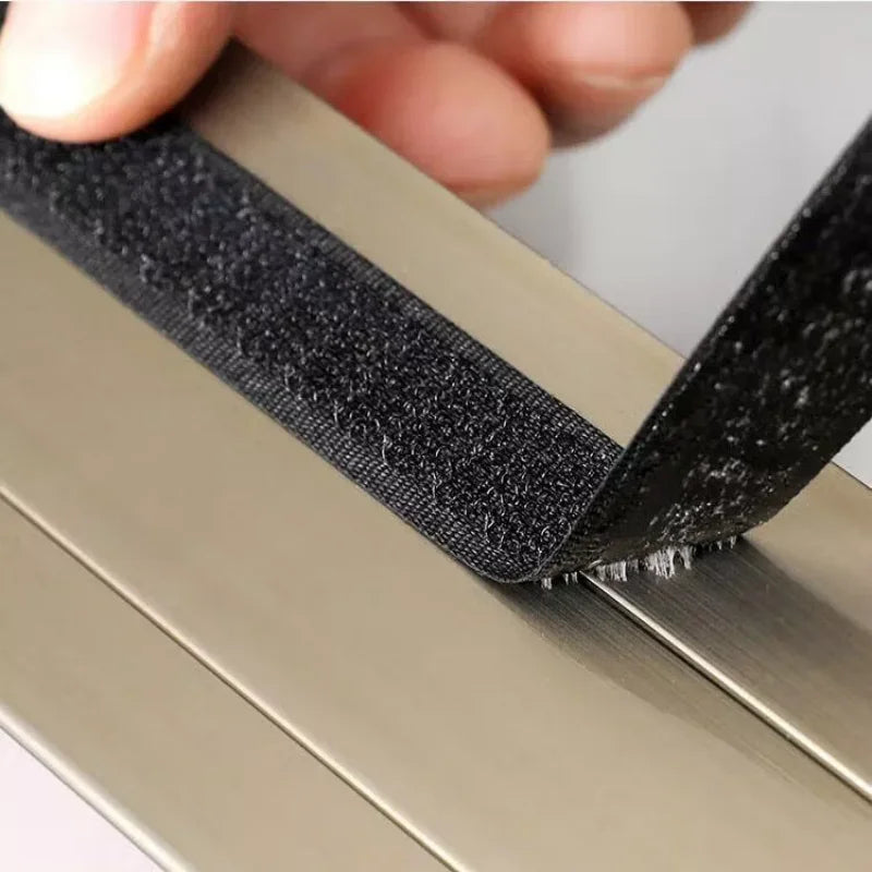 A hand is pulling a black self-adhesive window mosquito net screen across a metal frame.