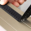 A hand is pulling a black self-adhesive window mosquito net screen across a metal frame.