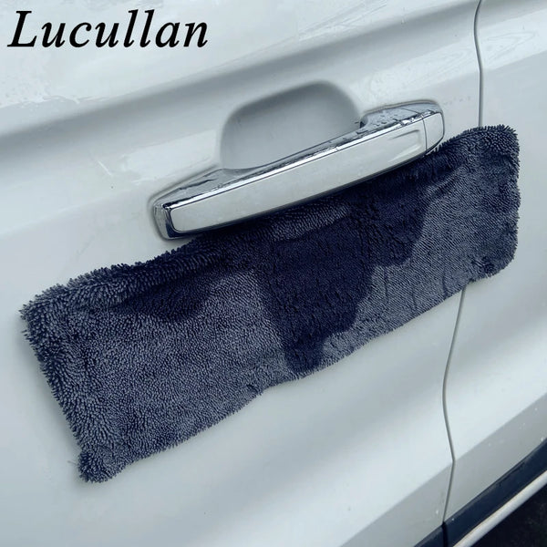 A dark gray microfiber drying towel is placed on a car door handle for cleaning.