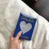 A hand holds a blue mini photo album titled COOL KIDS with a heart design against a white sheet.