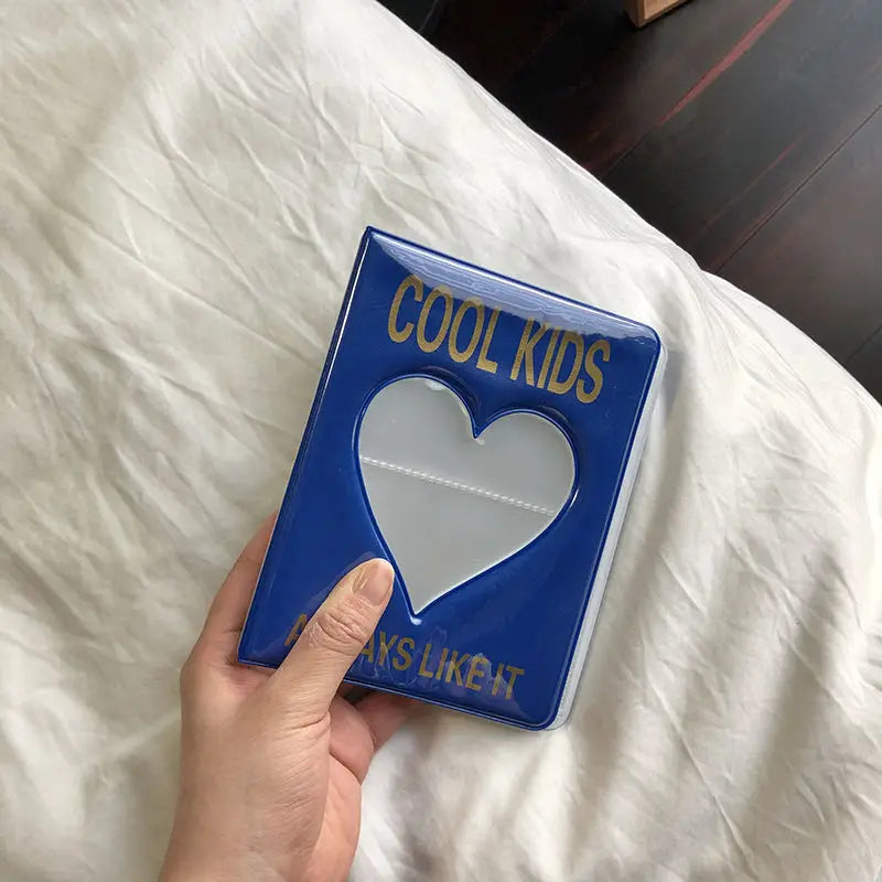 A hand holds a blue mini photo album titled COOL KIDS with a heart design against a white sheet.