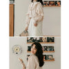 A woman models a white vintage lace long sleeve blouse against a light wall with framed photos.