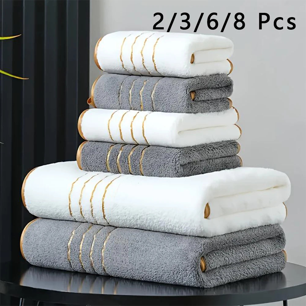A stack of luxury bath towels in white and gray with gold accents.