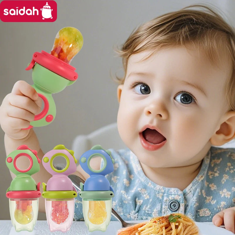 A baby is holding a green silicone fruit feeder with a dinosaur design, next to other colored feeders.