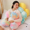 A person is lying down on a bed surrounded by various colorful, fluffy sunflower-themed plush pillows.