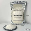 A clear plastic bag of 1000g natural soybean wax flakes next to a pile of white wax on a black plate.