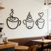 A set of three black iron art coffee cup wall decor pieces displayed on a white wall above a wooden counter.