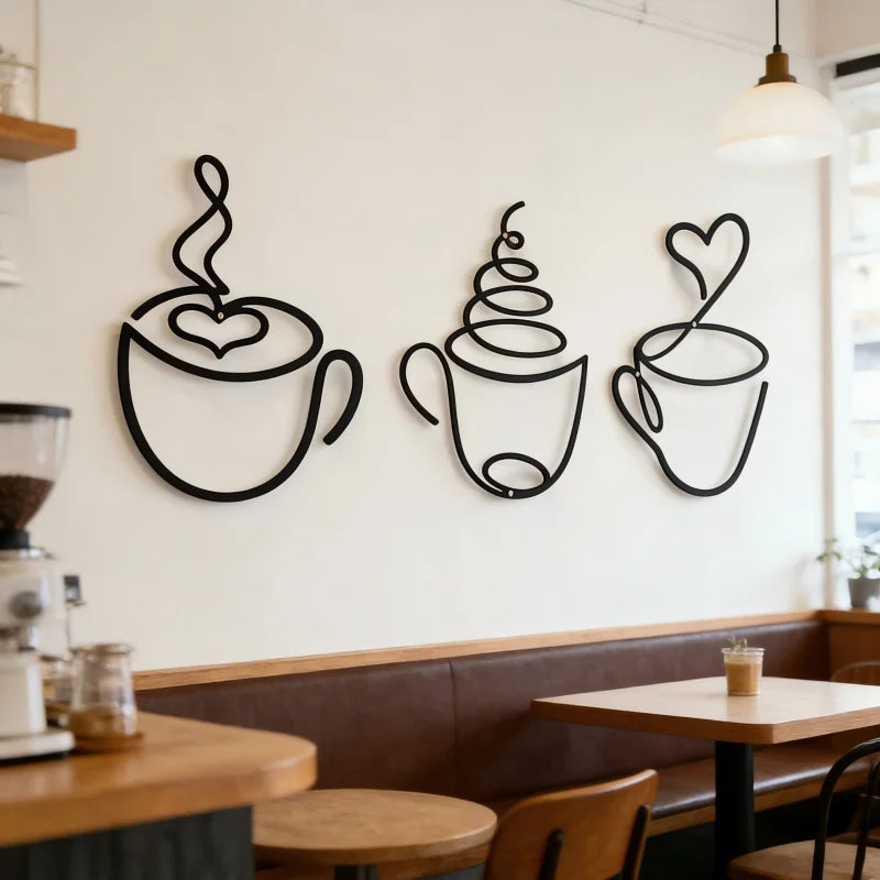 A set of three black iron art coffee cup wall decor pieces displayed on a white wall above a wooden counter.