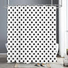 A white shower curtain with a black polka dot pattern hanging on a metal rod.