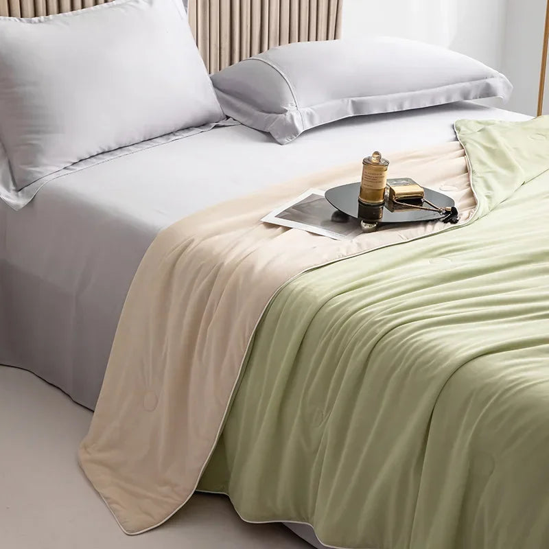 A light green cooling summer blanket is draped over a white bed with white pillows.