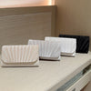 A display of elegant patent leather clutch bags in white and beige tones on a light wooden surface.