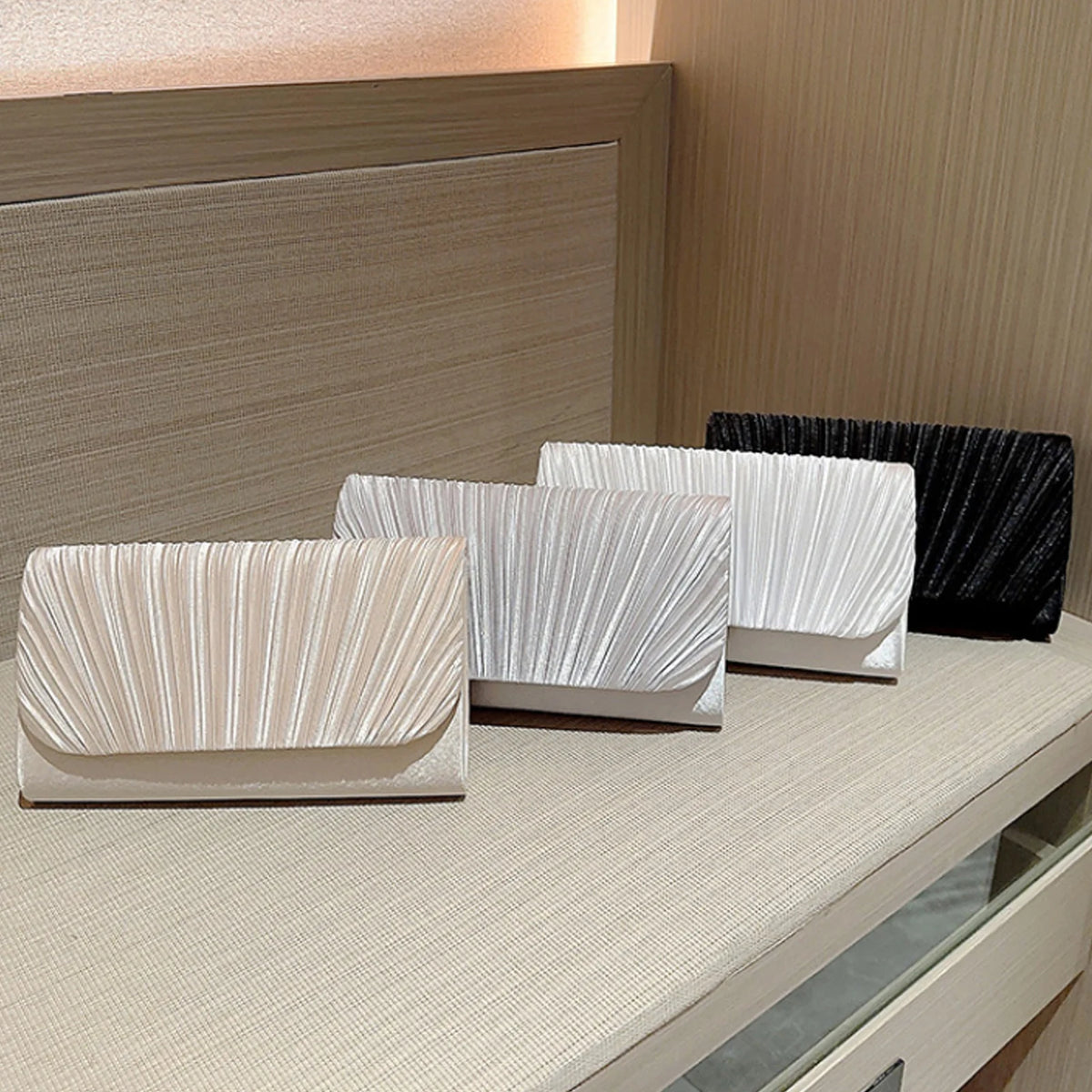 A display of elegant patent leather clutch bags in white and beige tones on a light wooden surface.