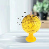 A yellow sticky fruit fly trap ball with a pink stick, showing small insects attracted to the surface.
