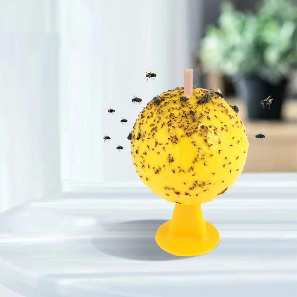A yellow sticky fruit fly trap ball with a pink stick, showing small insects attracted to the surface.
