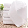 A stack of white soft cotton terry cloth face towels resting on a woven mat.