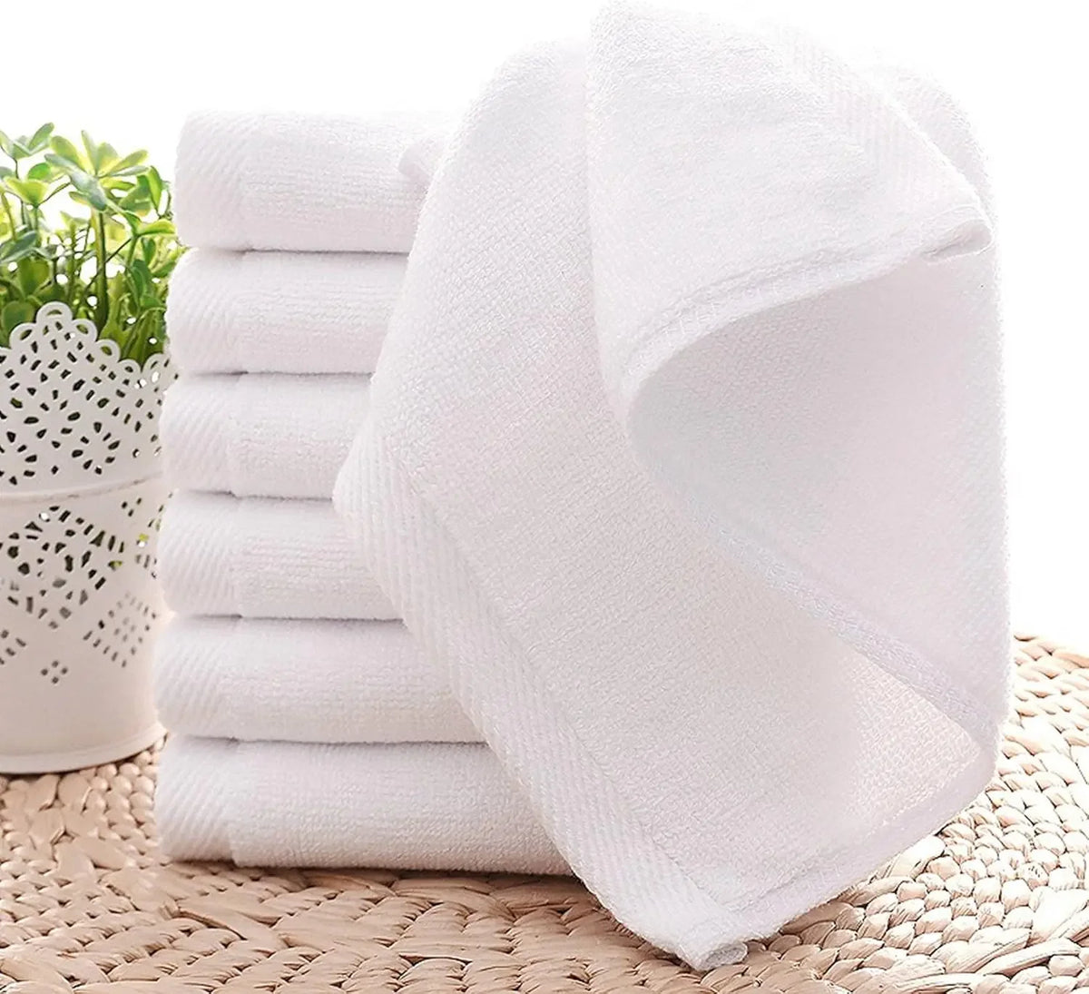 A stack of white soft cotton terry cloth face towels resting on a woven mat.