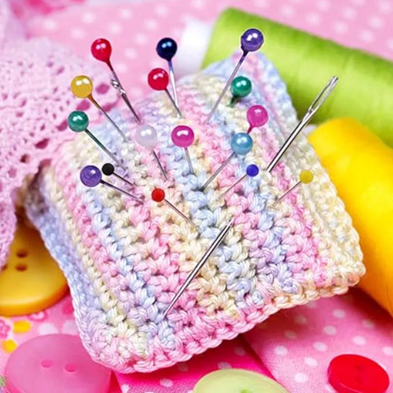 A pile of pearlized ball head sewing pins for fabric crafting resting on pink fabric.