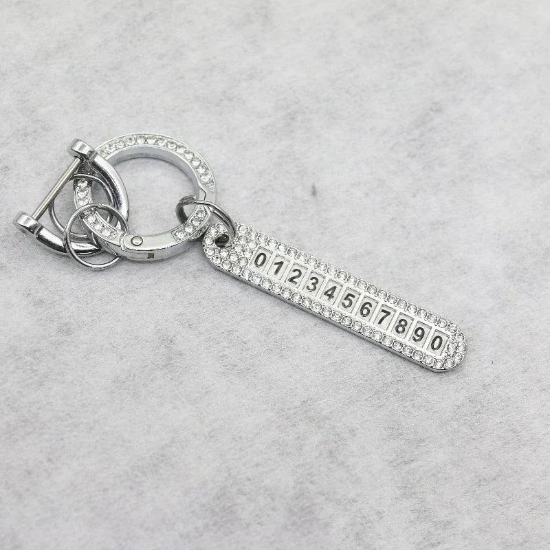 Silver key fob cover with a numbered plastic strip and a metal ring attached.