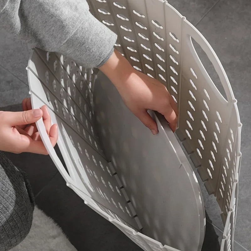 A person is holding a folding laundry basket with handles, showing the mesh interior and gray exterior.