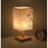 A Chinese style dimmable table lamp with a textured linen shade sits on a wooden base next to an analog clock.