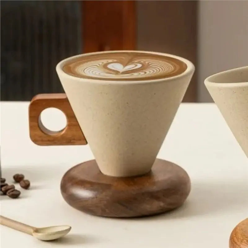 A ceramic coffee mug with latte art sits on a wooden base next to a spoon.