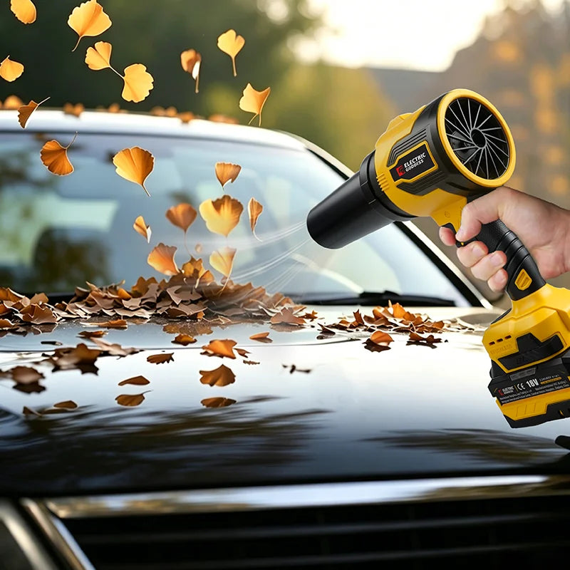 A hand uses a yellow cordless turbo leaf blower to clear autumn leaves from a car's hood.