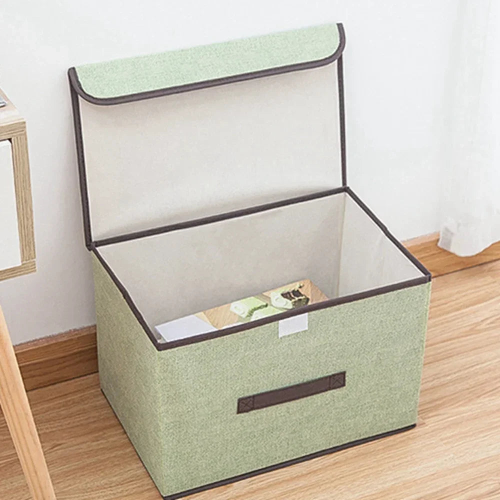 A light green fabric storage box with a hinged lid is shown on a wooden floor.