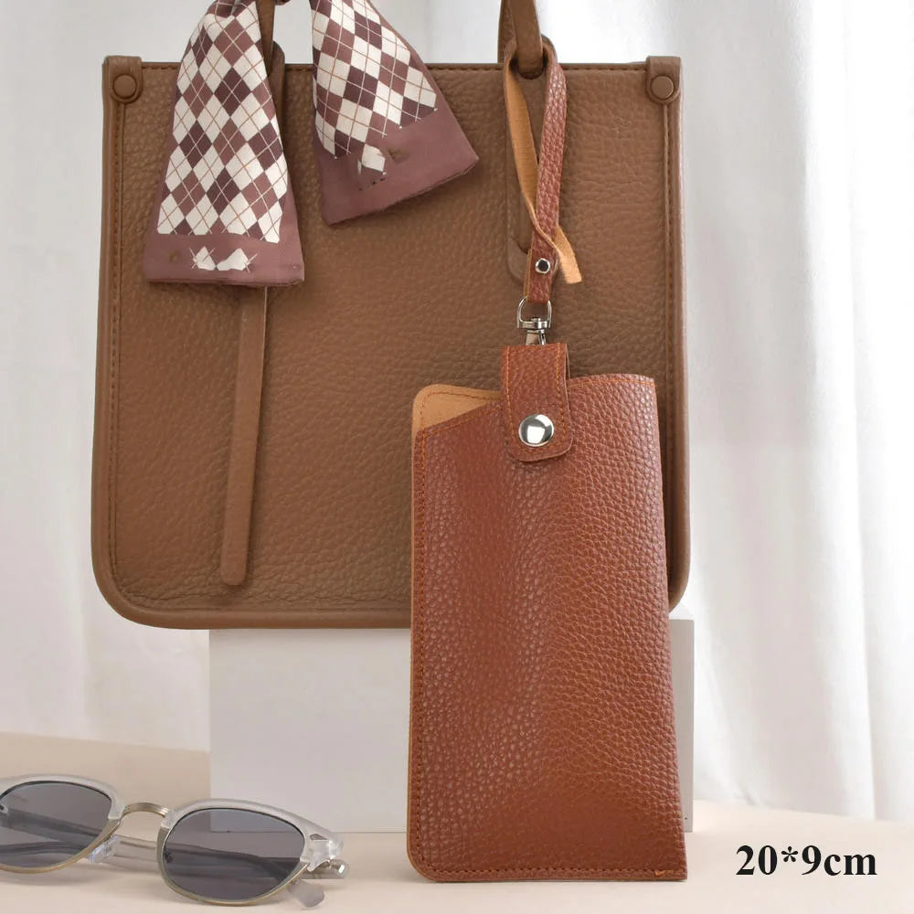 A brown leather glasses case with a checkered fabric strap and a matching leather pouch is displayed on a white surface.