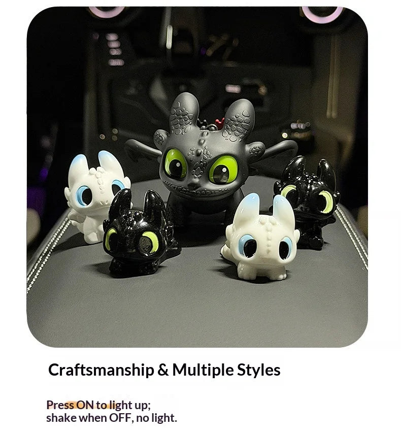 A collection of black and white Toothless-inspired charms with glowing eyes and movable wings displayed on a dark surface.