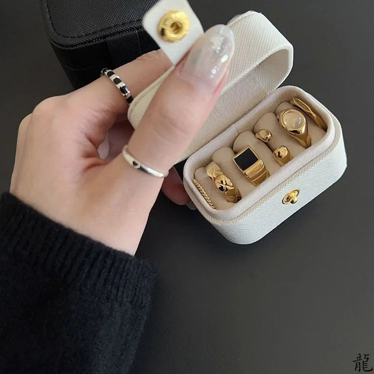 A hand holds an open cream-colored compact leather jewelry travel case filled with gold and silver rings and earrings.