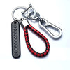 A silver keychain featuring a personalized phone number engraved on a tag and attached to a braided red and black leather rop