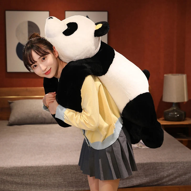 A young woman is posing with a giant black and white panda plush toy on a bed.