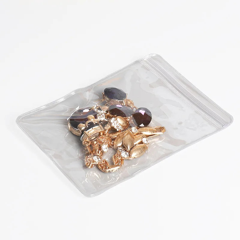 A clear plastic pouch with a zip lock closure containing a collection of gold-toned jewelry and dark colored stones.