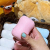 Eine Hand hält einen rosa Silikon-Stressball-Spielzeug neben ein gelbes Plüschtier und weiße Fidget-Bälle.