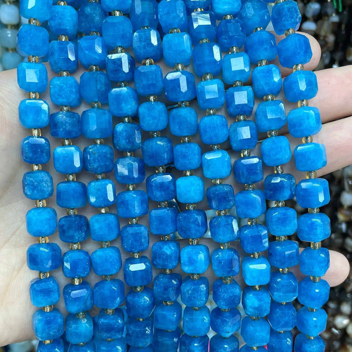 A hand holds a strand of bright blue natural stone square faceted beads for jewelry making.