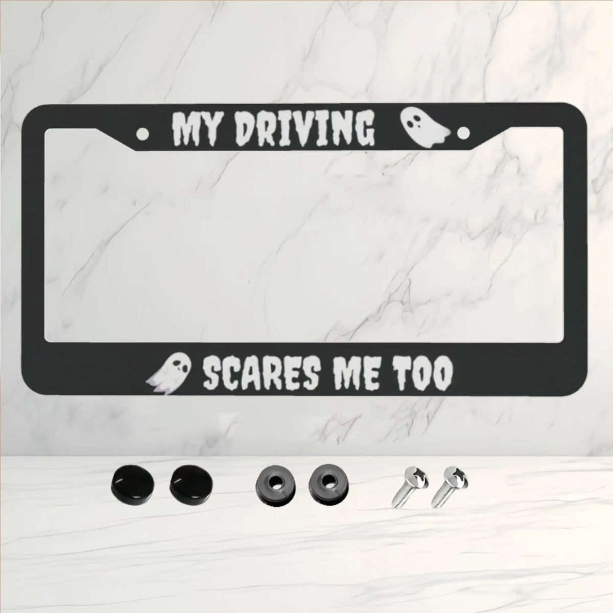A black license plate frame with the text My Driving scares me too and a ghost design on a white marble background.