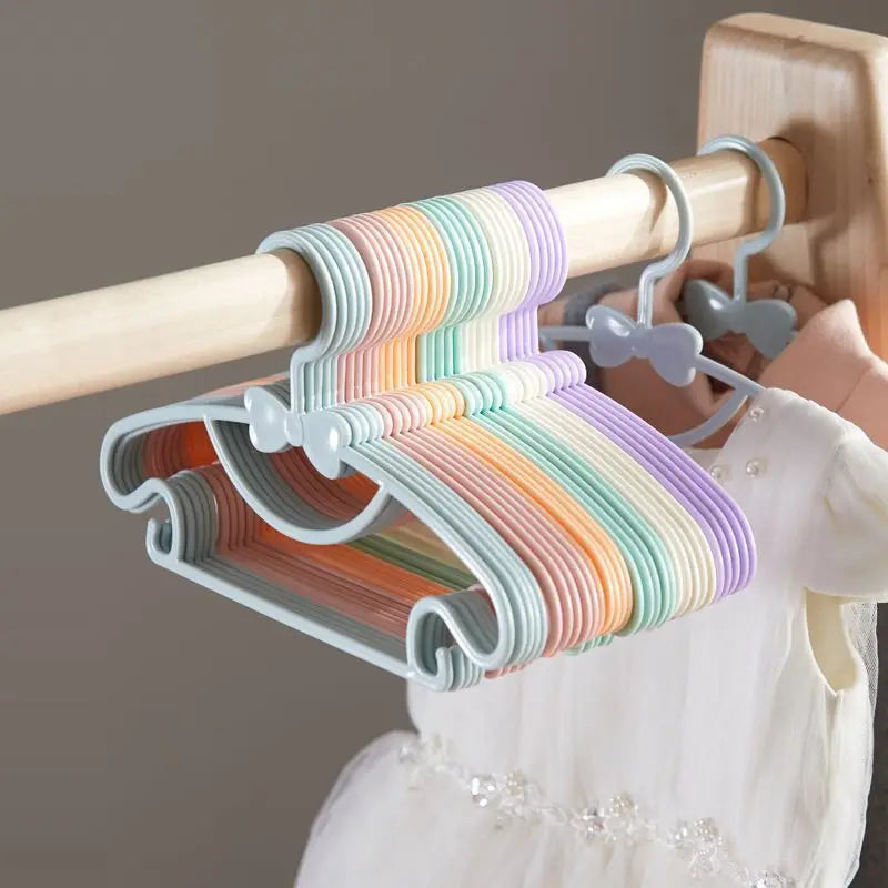 Colorful plastic hangers with bow designs hanging from a wooden rod.